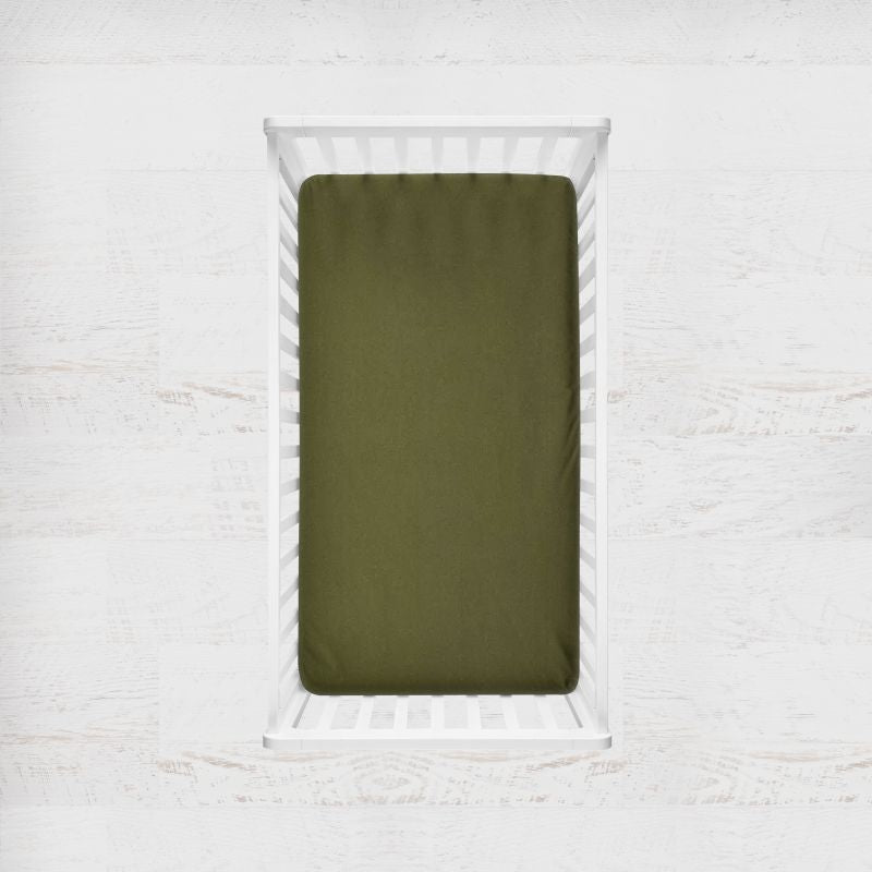 An avocado green fitted crib sheet shown inside a white wooden crib, set against a light, textured white wall background.
Avocado Green Crib Sheet - The Creative Raccoon 