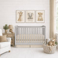 A styled nursery scene with a light gray wooden crib, beige bedding, a white armchair, a side table with a lamp and plant, and a wicker basket filled with stuffed animals. Above the crib are three framed animal prints showing a giraffe, a gray elephant named Henry, and a lion cub on a white shiplap wall.
 Baby Boy Crib Bedding Beige - The Creative Raccoon 