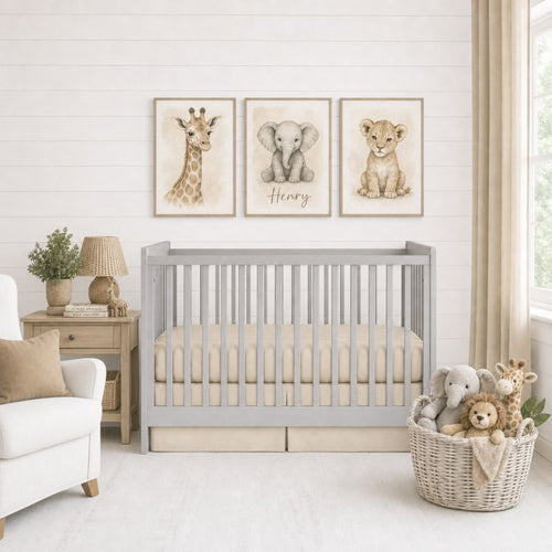 A styled nursery scene with a light gray wooden crib, beige bedding, a white armchair, a side table with a lamp and plant, and a wicker basket filled with stuffed animals. Above the crib are three framed animal prints showing a giraffe, a gray elephant named Henry, and a lion cub on a white shiplap wall.
 Baby Boy Crib Bedding Beige - The Creative Raccoon 