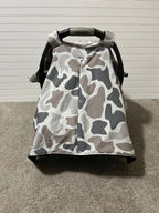 A baby car seat canopy cover with a gray, white, and brown camouflage pattern, draped over a black Graco car seat on a carpeted floor against a white paneled wall. Baby Car Seat Canopy Cover Camo - The Creative Raccoon