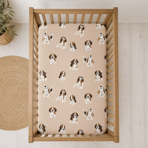A wooden crib viewed from above, fitted with a beige crib sheet printed with a repeating pattern of brown and white beagle dogs. The crib is placed on a light wood floor next to a woven jute rug.
Beagle Crib Sheet - The Creative Raccoon