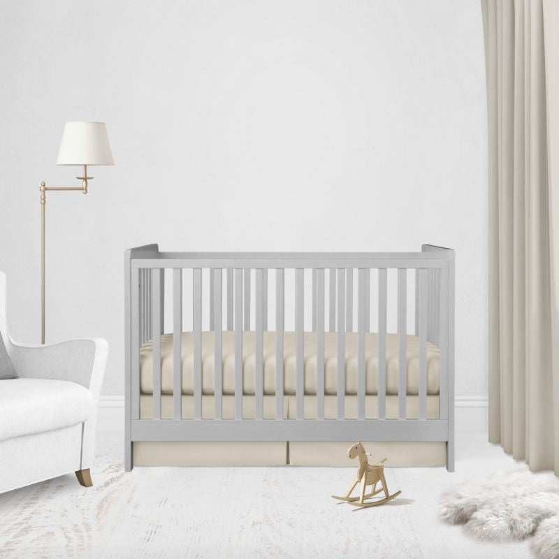 A light gray wooden baby crib with a beige mattress, styled in a bright, modern nursery with a white armchair, floor lamp, and beige curtains.
Beige Crib Sheet & Pleat Crib Skirt - The Creative Raccoon
