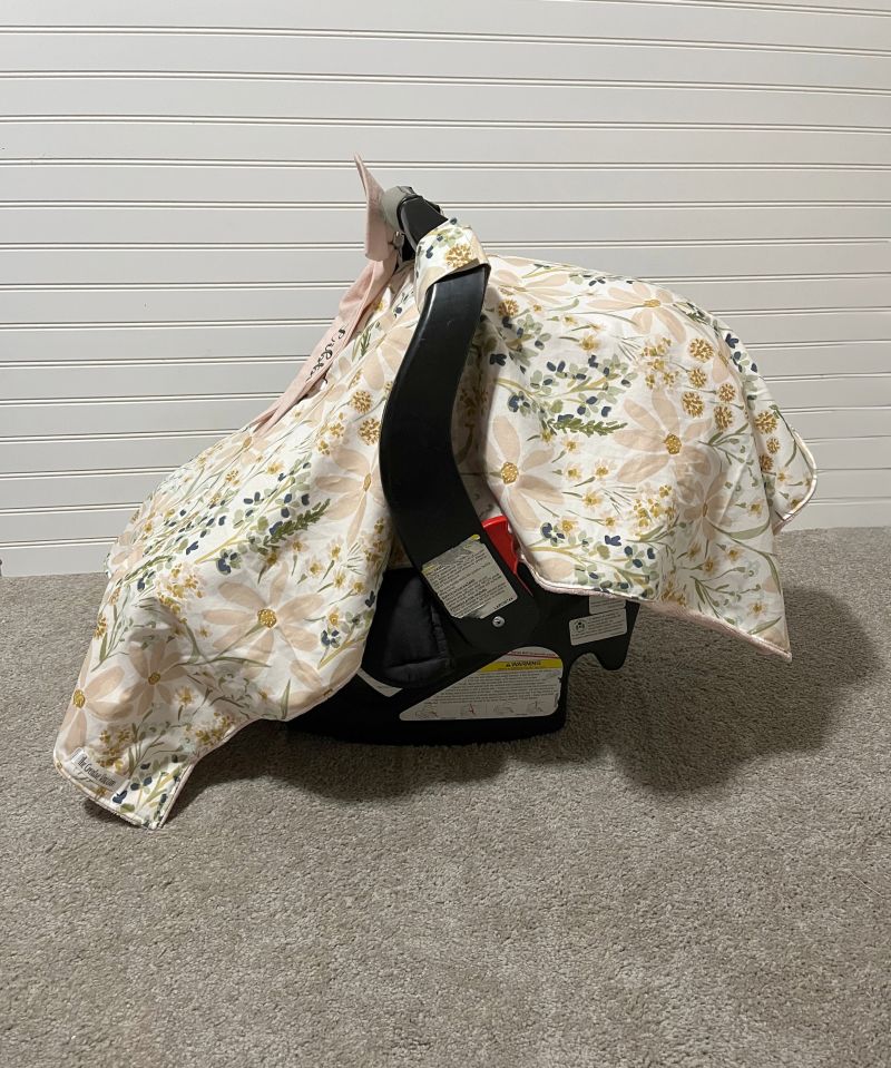 Floral-patterned cover on a baby car seat against a white wall. Car Seat Canopy Daisy - The Creative Raccoon