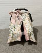 Floral baby car seat cover with pink bow and name on a gray floor. Car Seat Canopy Daisy - The Creative Raccoon