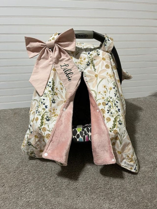Floral car seat cover with pink bow and 'Bella' embroidery on a gray floor. Car Seat Canopy Daisy - The Creative Raccoon