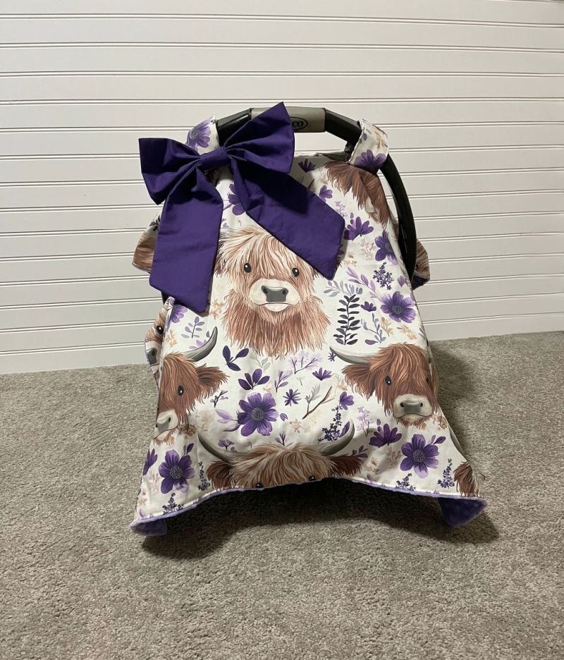 Car seat cover with Highland cow pattern and purple bow on a neutral background & a purple bow. Car Seat Canopy Highland Cows - The Creative Raccoon