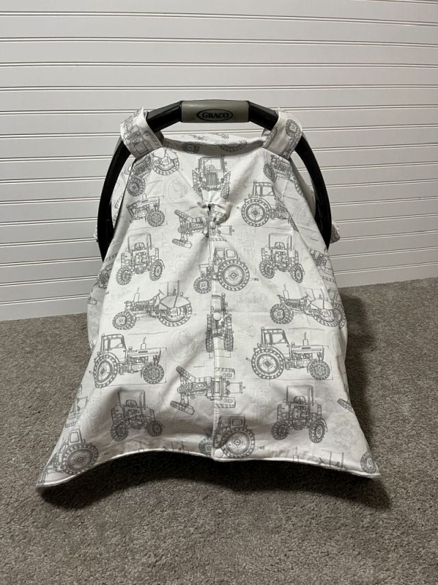 Baby car seat cover with tractor pattern on a carpeted floor. Car Seat Canopy Tractors - The Creative Raccoon