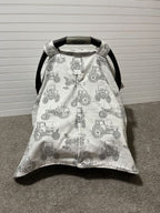 Baby car seat cover with tractor pattern on a carpeted floor. Car Seat Canopy Tractors - The Creative Raccoon