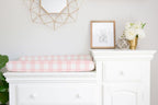 White dresser with pink checkered changing pad, framed picture, and decorative items in a nursery. Changing Pad Cover Light Pink Gingham - The Creative Raccoon
