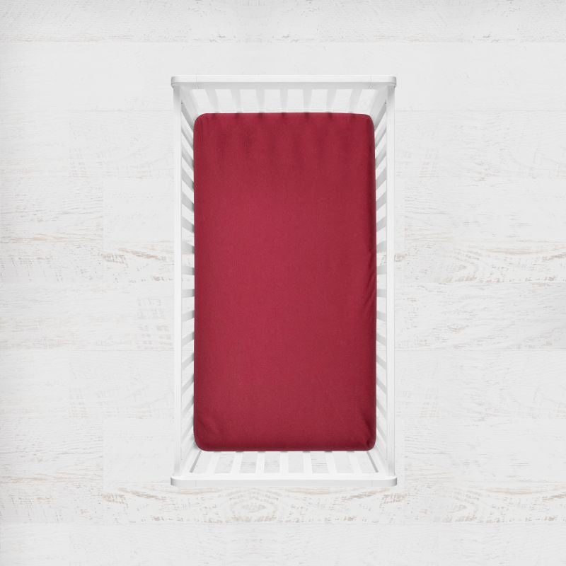 Red fitted sheet on a white bed frame against a white textured wall. claret red crib sheet - the creative raccoon