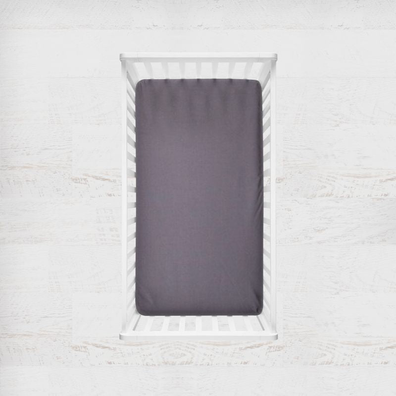 A dark coal gray fitted crib sheet displayed inside a white wooden baby crib, viewed from directly above against a light textured wall. Coal Gray Crib Sheet - The Creative Raccoon