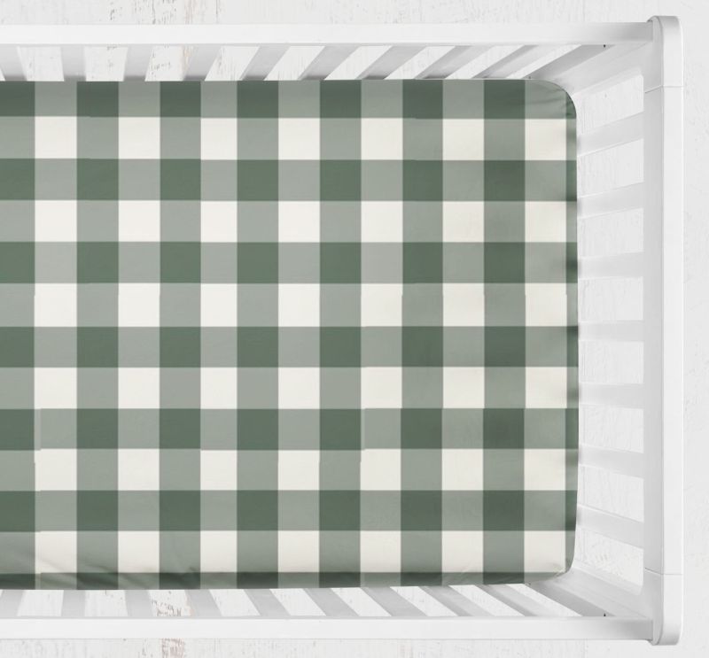 A fitted crib sheet with a green and white gingham check pattern, shown inside a white wooden crib. Crib Sheet - Dark Sage gingham - The Creative Raccoon