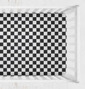 A black and white checkered crib sheet shown from above inside a white crib. Crib Sheet Black and White Checkered - The Creative Raccoon