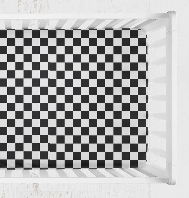 A black and white checkered crib sheet shown from above inside a white crib. Crib Sheet Black and White Checkered - The Creative Raccoon