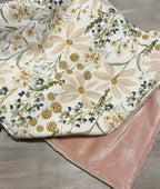 Floral-patterned blanket with pink backing on a wooden surface. Daisy Baby Blanket - The Creative Raccoon