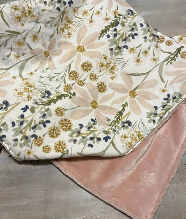 Floral-patterned blanket with pink backing on a wooden surface. Daisy Baby Blanket - The Creative Raccoon