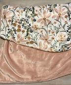 Floral-patterned blanket with pink backing on a wooden surface. Daisy Baby Blanket - The Creative Raccoon