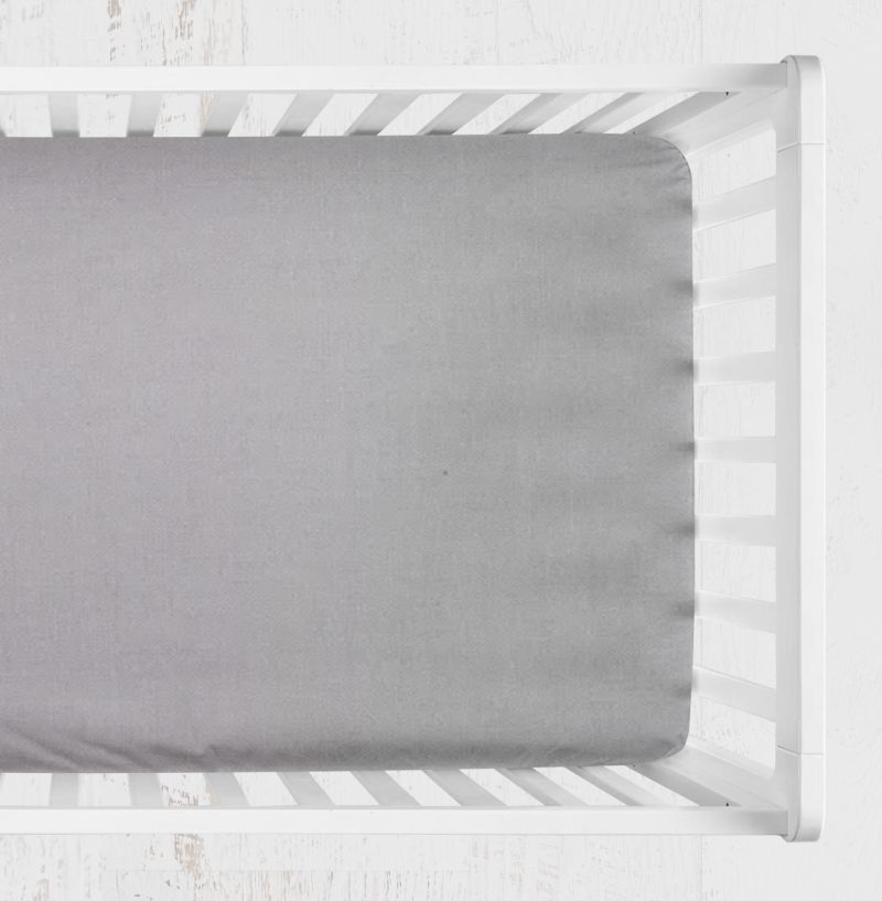 A light gray fitted crib sheet shown from above inside a white wooden crib on a white textured background.