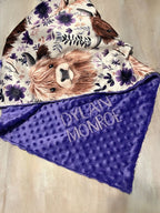 Blanket with highland cow design and floral patterns, featuring the name 'Dylain Monroe' on a purple background. Highland Cow Baby Blanket - The Creative Raccoon