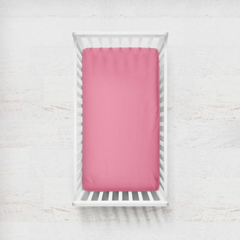 A hot pink fitted crib sheet displayed on a mattress inside a white wooden crib, set against a light, textured white wall background. Hot Pink Crib Sheet - The Creative Raccoon