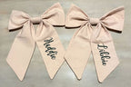 Two blush pink fabric bows with long tails, each embroidered baby's name. 
 Large Personalized Bow, Accessory - The Creative Raccoon