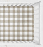 A fitted crib sheet with a classic brown and white gingham check pattern, shown inside a white wooden crib. Khaki Gingham Crib Sheet 2 inch squares - The Creative Raccoon