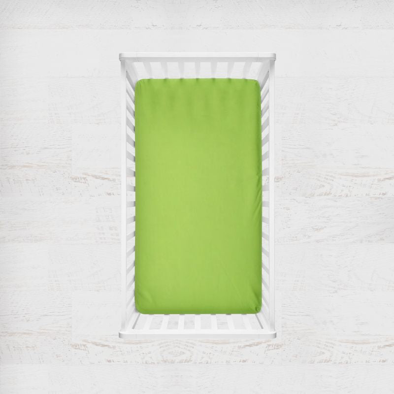 A bright lime green fitted sheet on a mattress inside a white wooden baby crib, shown from a top-down view against a white textured background. Kiwi Lime Green Crib Sheet - The Creative Raccoon