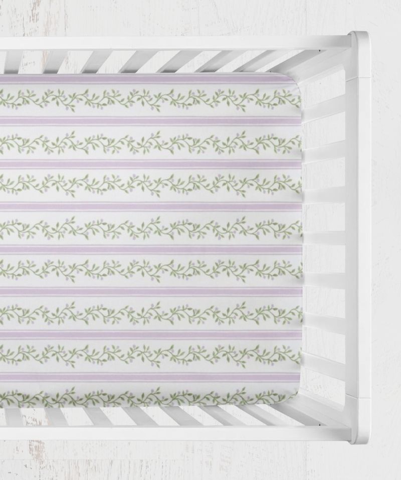 A close-up view of a fitted crib sheet featuring horizontal lavender stripes and green leafy vine patterns, shown inside a white wooden crib. Libby Purple & Green Stripes & Vines Crib Sheet - The Creative Raccoon