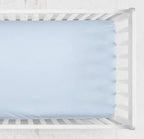 A light blue fitted crib sheet shown from above inside a white wooden crib. Light Blue Crib Sheet - The Creative Raccoon