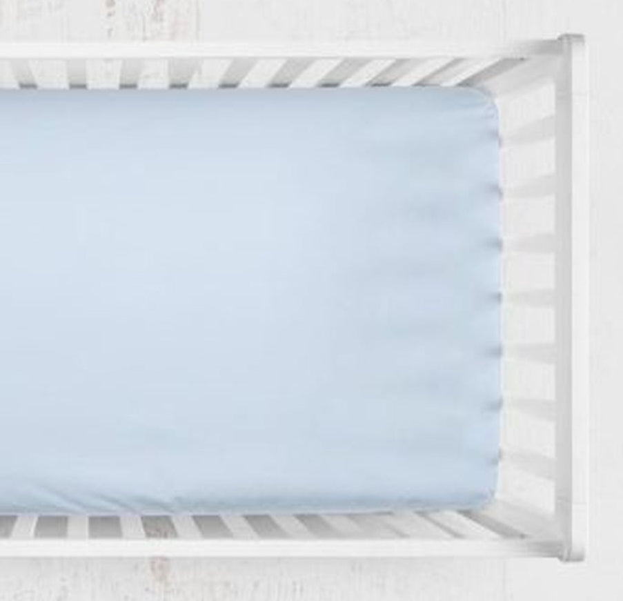 A light blue fitted crib sheet shown from above inside a white wooden crib. Light Blue Crib Sheet - The Creative Raccoon