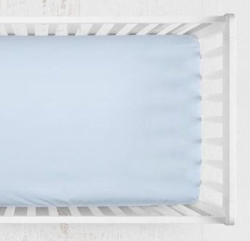 A light blue fitted crib sheet shown from above inside a white wooden crib. Light Blue Crib Sheet - The Creative Raccoon