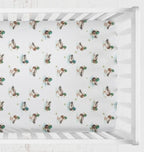 A white crib fitted sheet with a repeating pattern of mallard ducks, shown inside a white wooden crib. Mallard Duck Crib Sheet - The Creative Raccoon