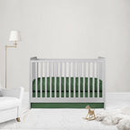 A white wooden baby crib with a dark green fitted sheet and matching green skirt, styled in a minimalist nursery with a white armchair, gold floor lamp, and wooden rocking horse.
Pesto Green Crib Sheet & Crib Bed Skirt - The Creative Raccoon