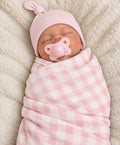 Baby wearing a solid light pink knot hat and wrapped in a light pink and white checkered swaddle
