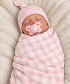 Baby wearing a solid light pink knot hat and wrapped in a light pink and white checkered swaddle