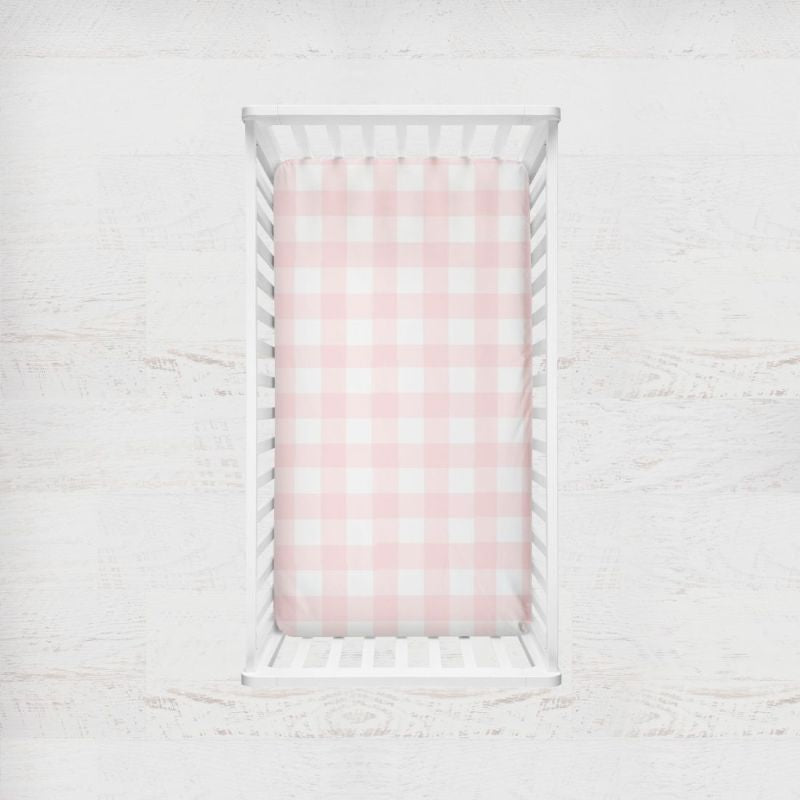 Crib with pink and white checkered fitted sheet on a light wooden floor.
Pink Gingham Crib Sheet - The Creative Raccoon