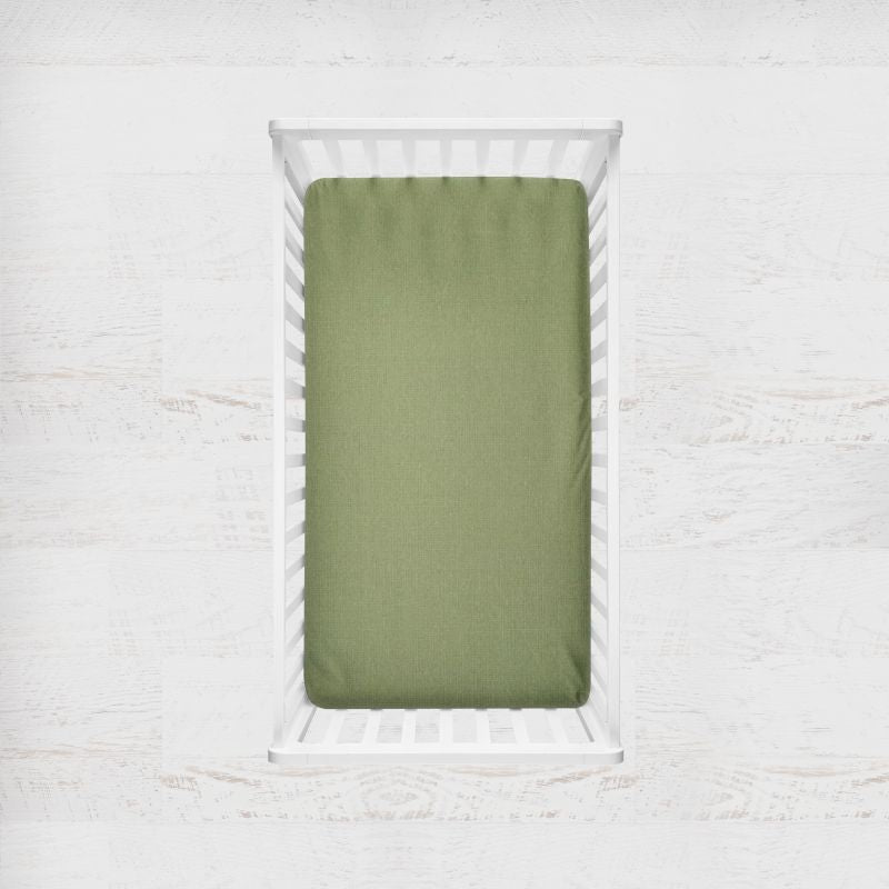 An seafoam green fitted crib sheet shown inside a white wooden crib, set against a light, textured white wall background. Seafoam Green Crib Sheet - The Creative Raccoon