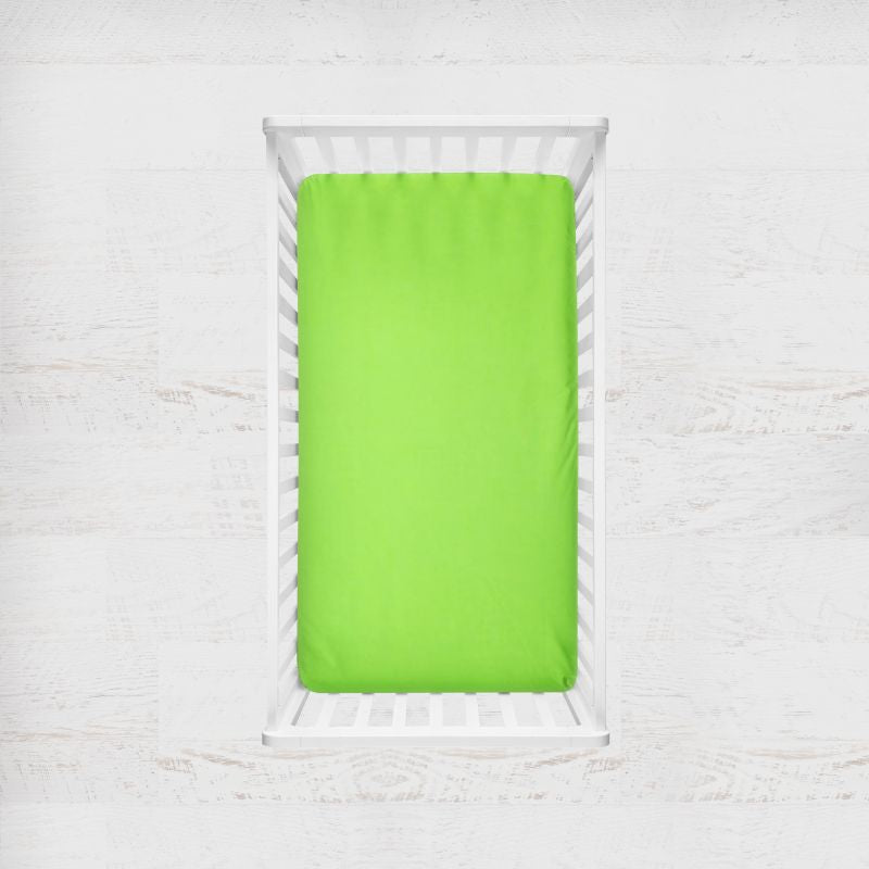 A bright lime green fitted sheet on a mattress inside a white wooden crib, shown from a top-down view against a white textured background. Sour Apple Lime Green Crib Sheet - The Creative Raccoon