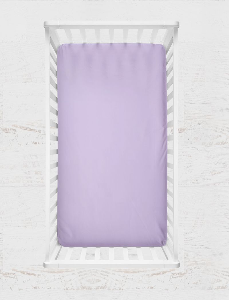 A lavender purple fitted sheet displayed inside a white wooden baby crib, shown from a top-down view against a light, textured background. Thistle Light Purple Crib Sheet - The Creative Raccoon