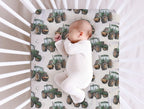A sleeping newborn baby in a white footed onesie lies on a fitted crib mattress with a green tractor patterned cover, photographed from above inside a white crib.
Tractor Crib Sheet with Cream Background - The Creative Raccoon