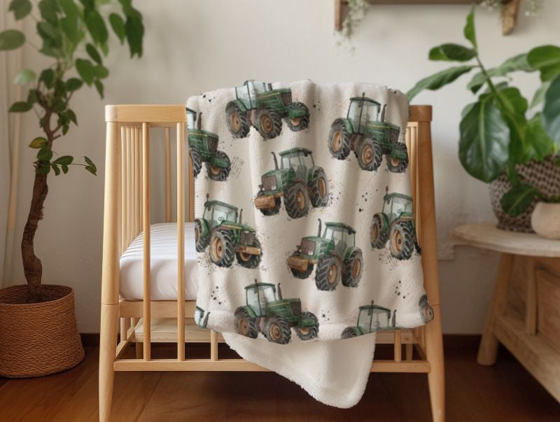 A soft minky fleece blanket featuring a repeating pattern of green farm tractors on a cream background, draped over a light wood crib in a styled nursery setting with potted plants.
Tractor Minky Blanket with Cream Background - The Creative Raccoon