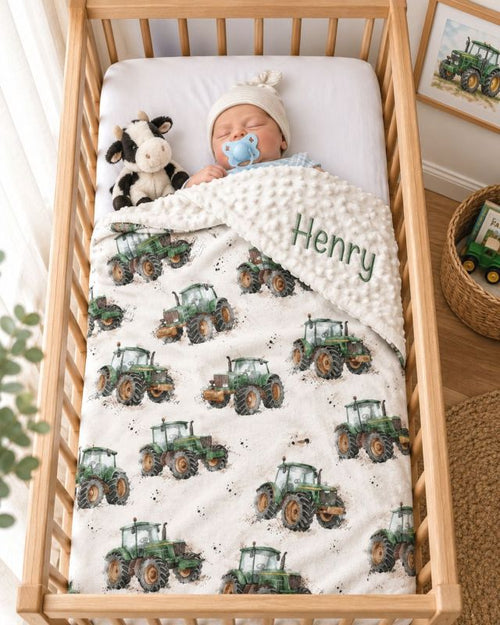 A baby sleeping in a wooden crib, wrapped in a personalized cream blanket printed with green tractor illustrations and the name 'Henry' embroidered on the corner. The baby wears a white knit hat and has a blue pacifier, with a plush cow toy beside them. Tractor Minky Blanket with Cream Background - The Creative Raccoon