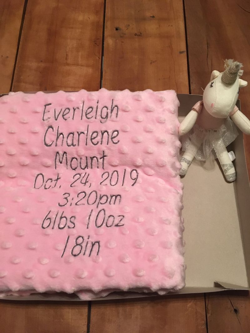 Pink blanket with baby birth details on a wooden floor with a unicorn toy. - the creative raccoon