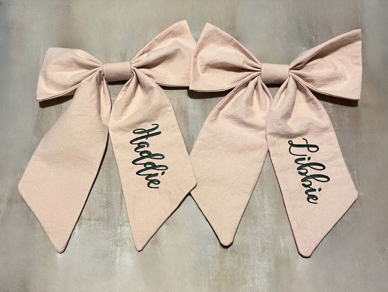 Two pink bows with names written on them against a gray background