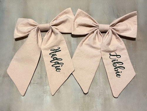 Two pink bows with names written on them against a gray background
