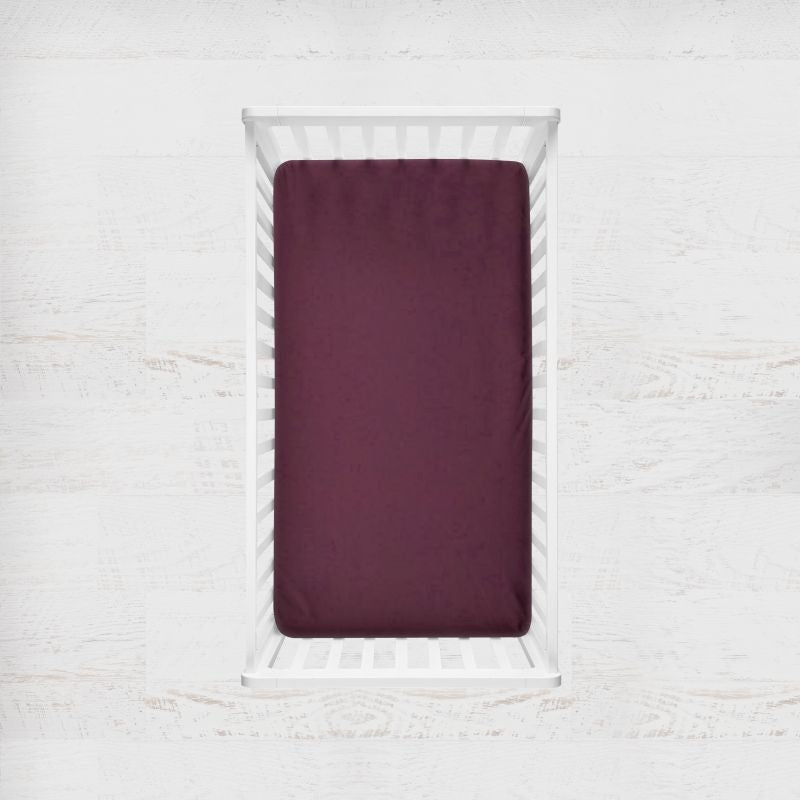 burgundy fitted crib sheet on a white baby bed against a light gray background. Burgundy crib sheet - the creative raccoon