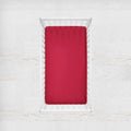 Red fitted sheet on a white bed with a white background. cardinal crib sheet - the creative raccoon