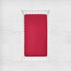 Red fitted sheet on a white bed with a white background. cardinal crib sheet - the creative raccoon