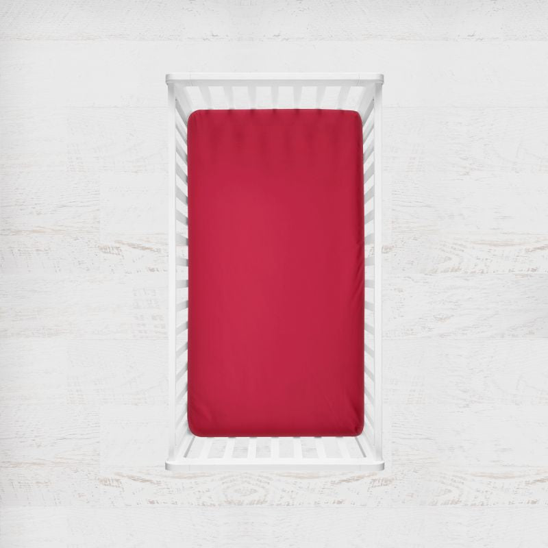 Red fitted sheet on a white bed with a white background. cardinal crib sheet - the creative raccoon