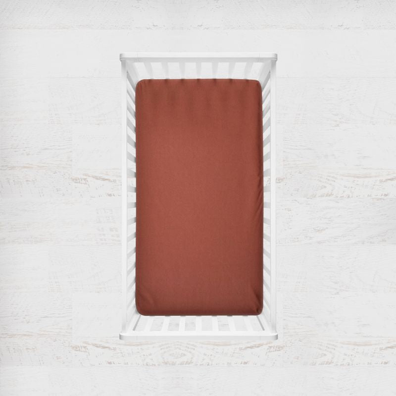 Copper fitted sheet on a white bed frame against a light gray background. copper crib sheet - the creative raccoon